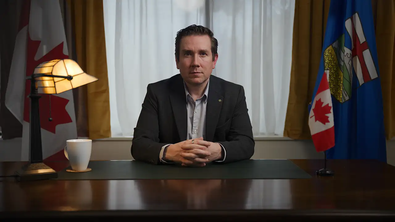 MP Corey Hogan at his desk between Canadian and Alberta flags, preparing to record a rapid-response video.